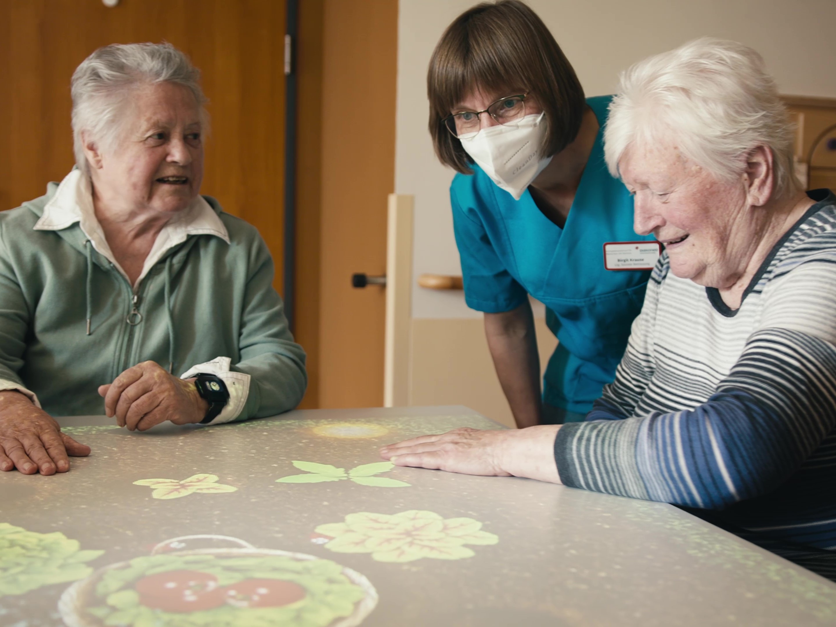 Seniorinnen mit Pflegefachperson bei einem digitalen Spiel am Tisch